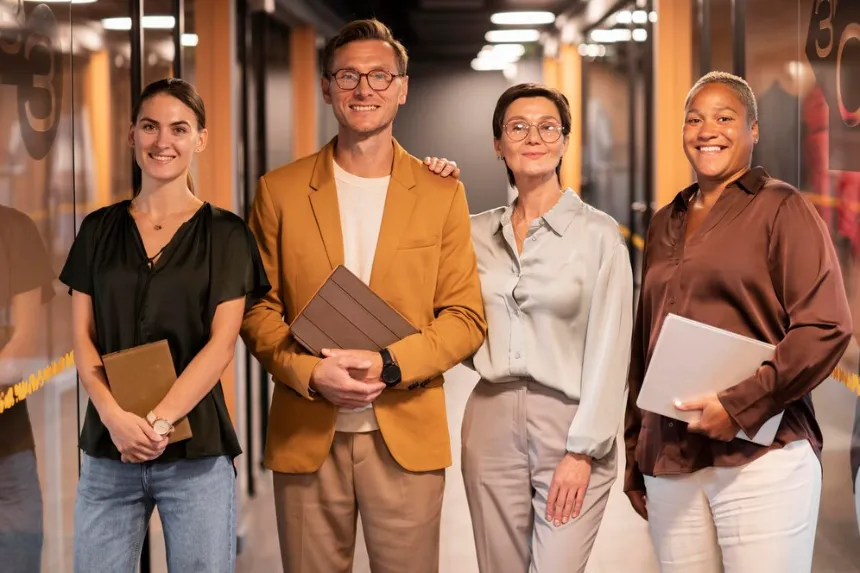 Confident four‑person team smiles in office corridor, sharing tablets and ready for growth thanks to our business directory